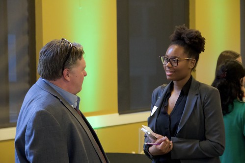 A man and young woman talk in front of two windows.